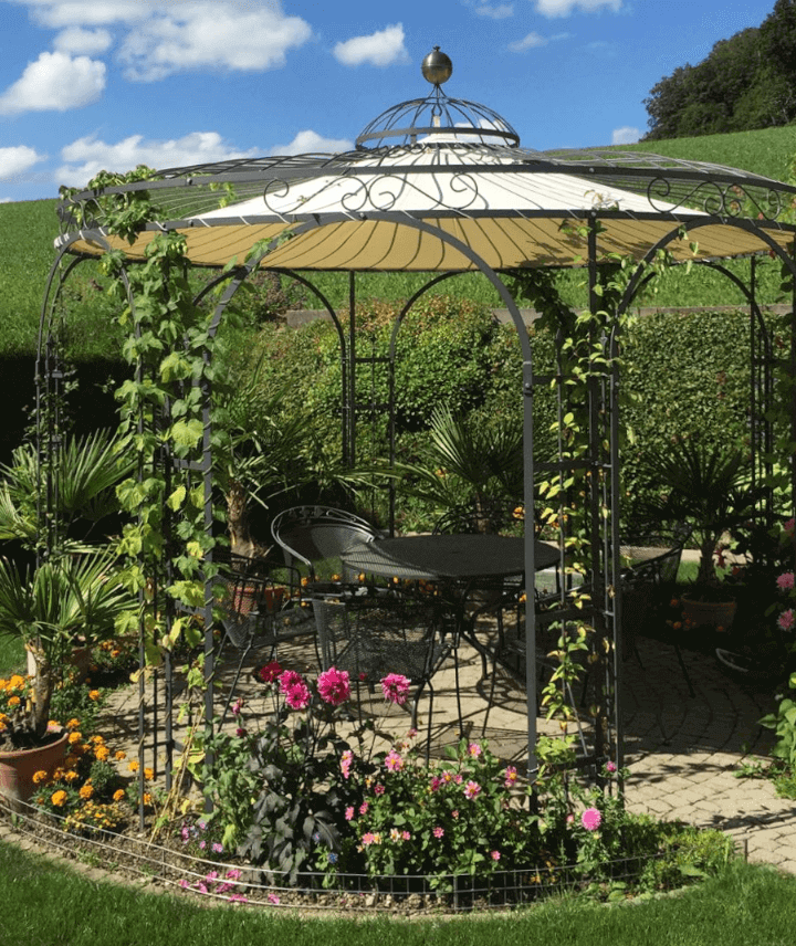 anthrazit-farbiger Gartenpavillon mit Pflanzen berankt und umrandet