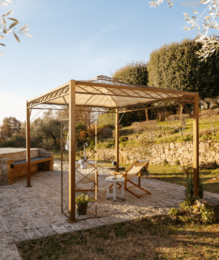 Tonnelle ELEO Trento intégrée dans le jardin sur une terrasse pavée. 