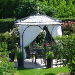 Gloriette ELEO Milano dans un jardin, avec voile d’ombrage et rideaux